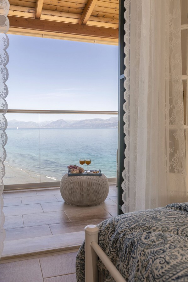 A bedroom with a view of a lake, a bed, a bedside table with glasses and pastries, and a woven ottoman.