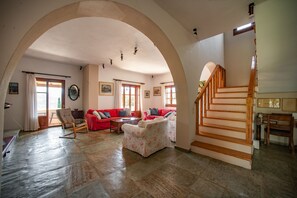 A spacious living room with a high arched ceiling, a staircase, and a red sofa set. - Alisachni Apartments (Corfu)