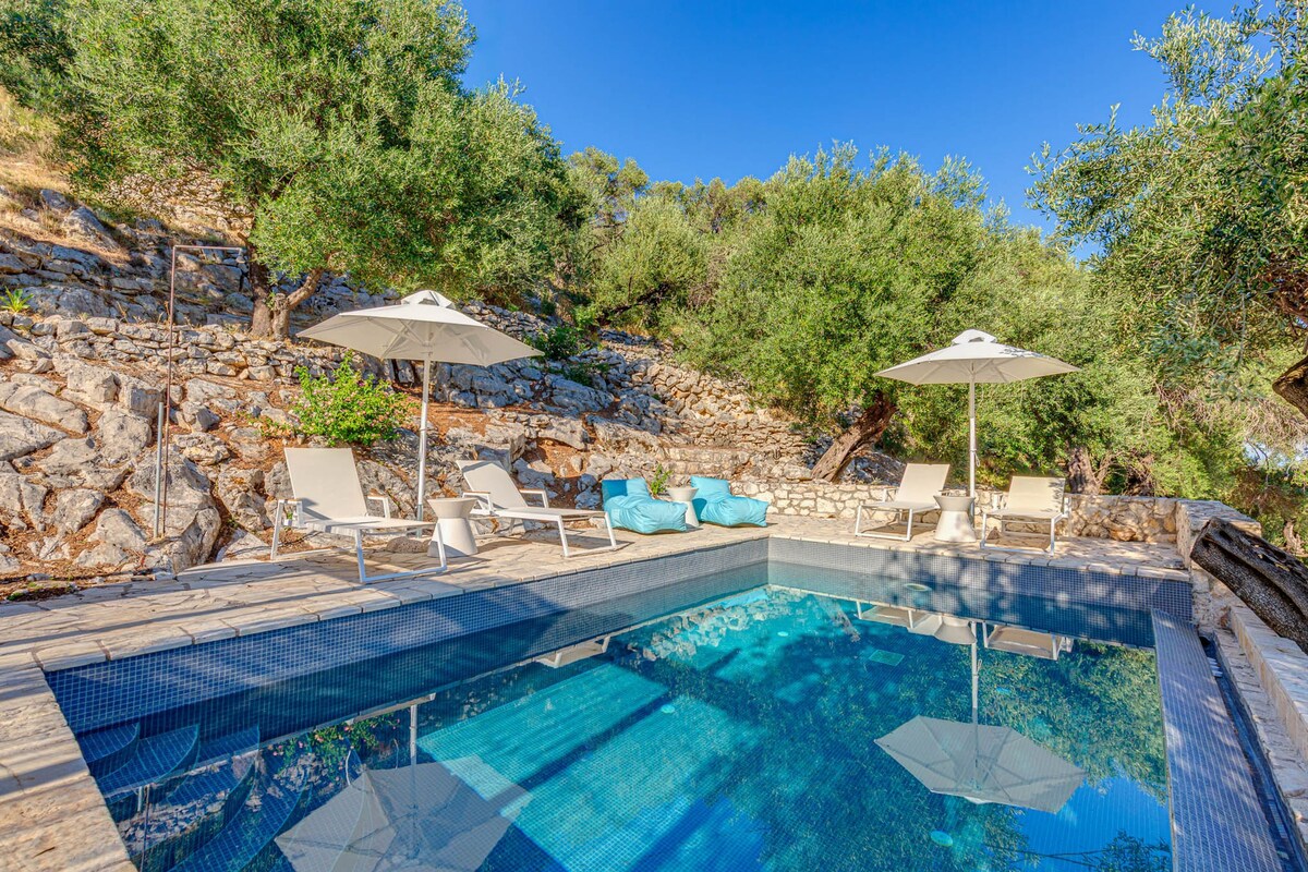 A pool area with clear blue water, stone walls, and lounge chairs.