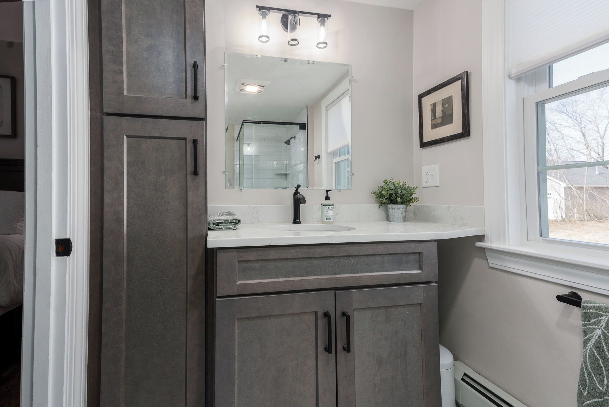 Une salle de bain avec un grand miroir, un lavabo avec un distributeur de savon et une fenêtre.