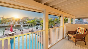 A balcony with a wicker chair and a view of a swimming pool and waterfront.