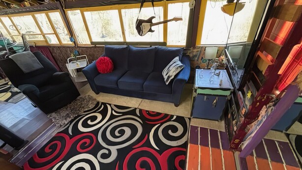 Una sala acogedora con un sofá azul, un cojín rojo y un tapete estampado.