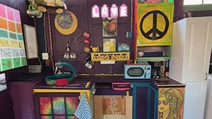 Una habitación colorida y ecléctica con diversas decoraciones, incluyendo un símbolo de paz, un microondas y varias obras de arte.