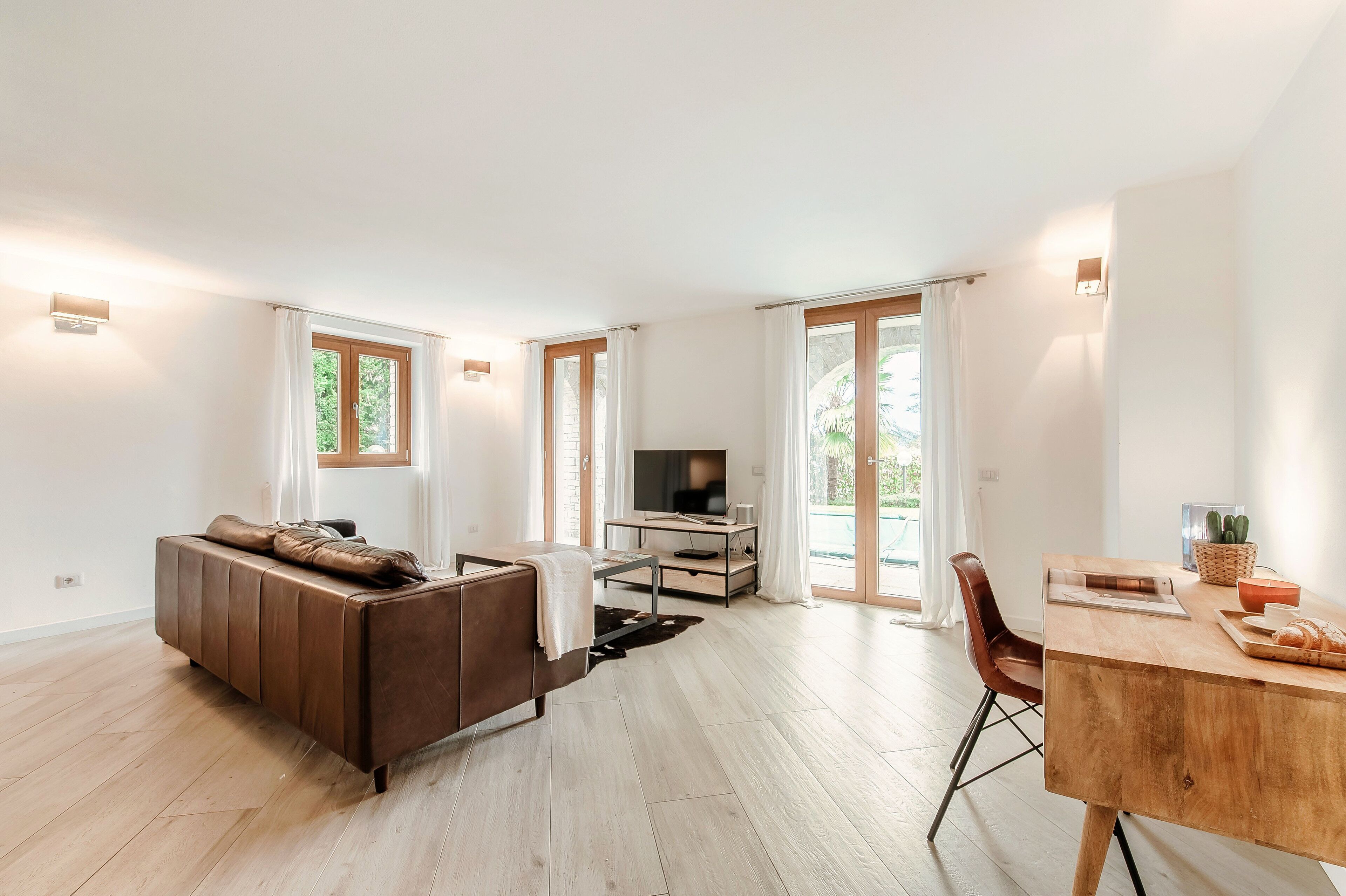 A modern living room with a sofa, TV, dining table, and large windows.