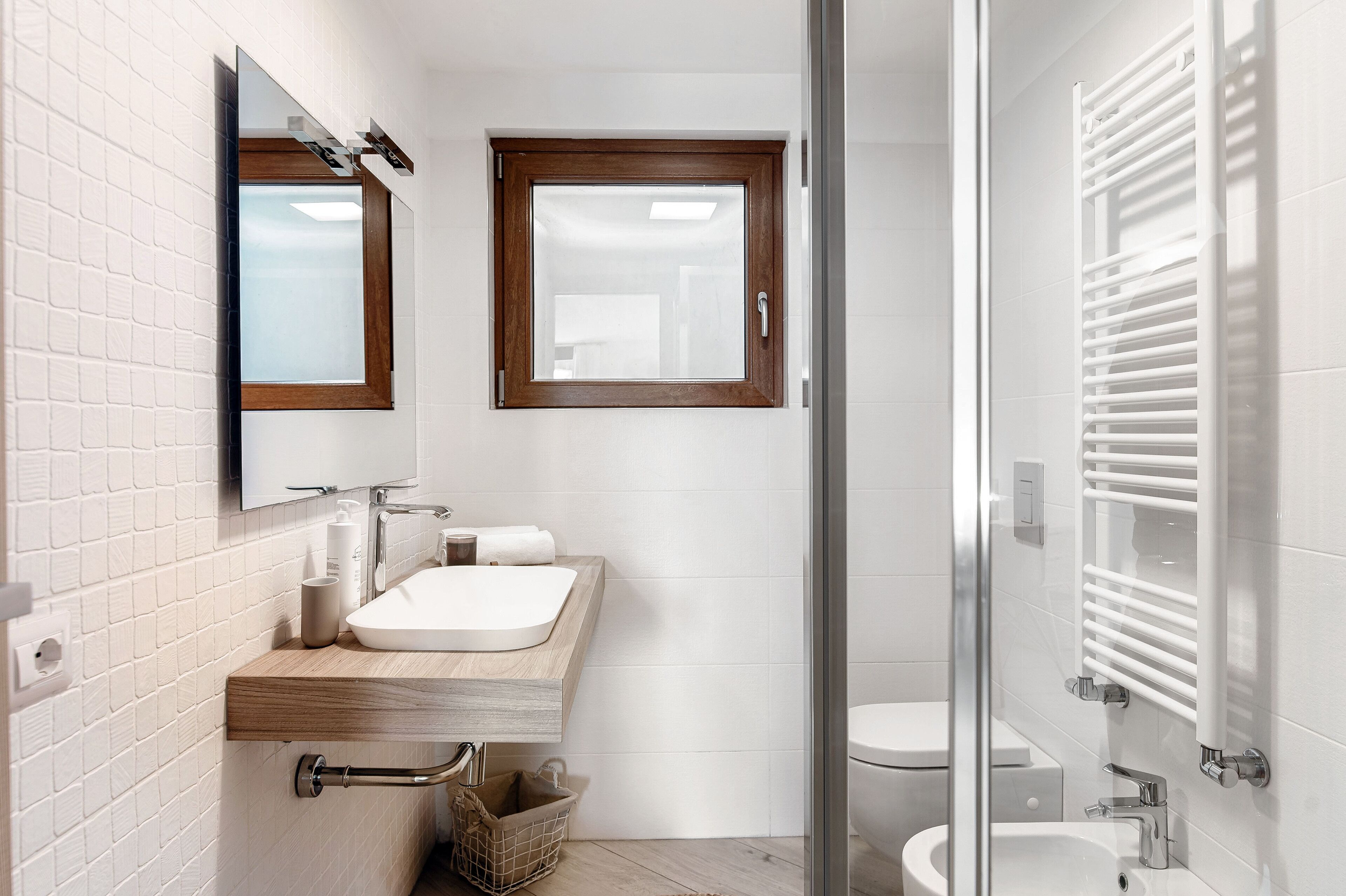 Een moderne badkamer met een houten wastafelmeubel, een grote spiegel, een raam en een douchecabine van glas.
