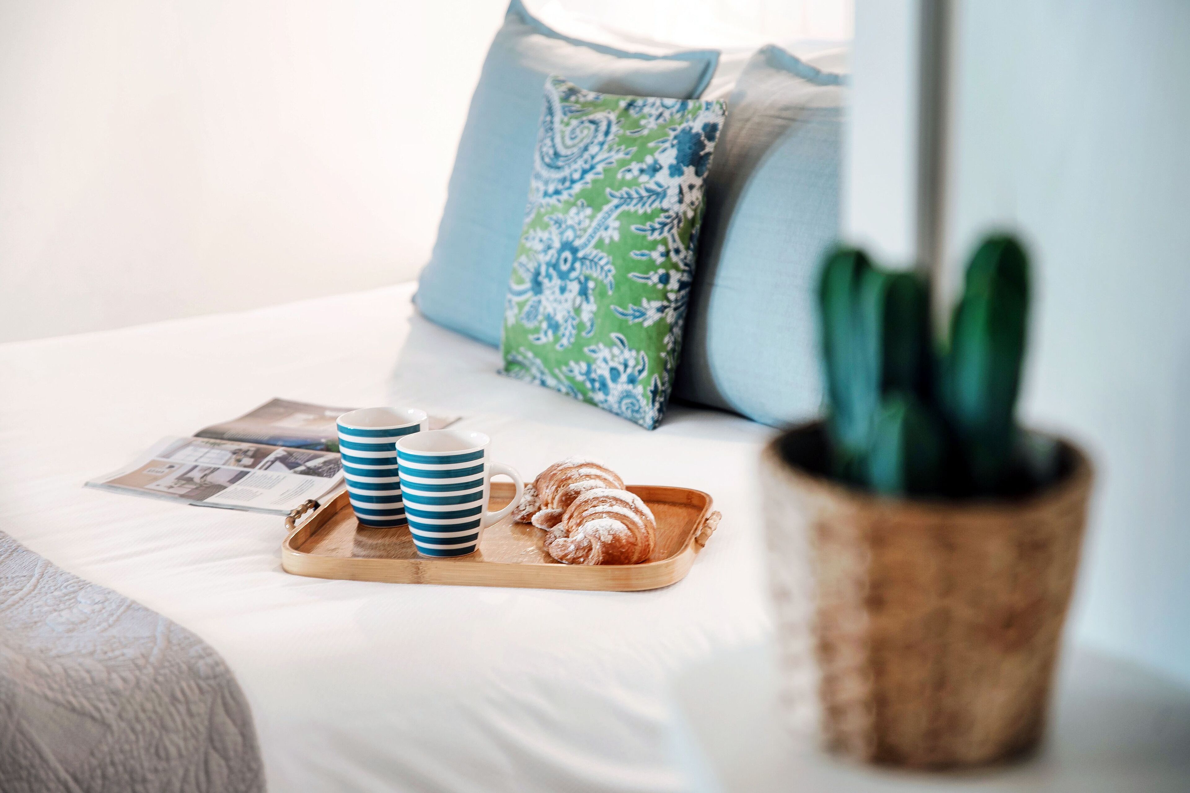 Een net opgemaakt bed met een schaal croissants, een tijdschrift en twee gestreepte mokken.