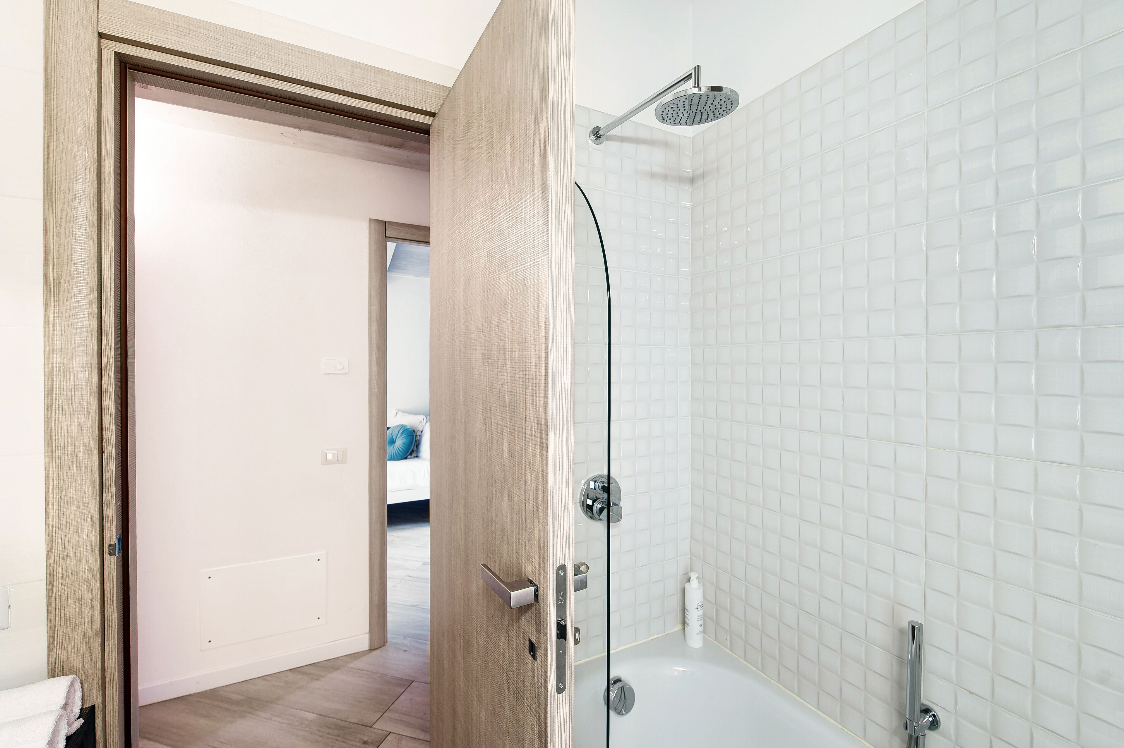A modern bathroom with a glass-enclosed shower, a white tiled wall, and a wooden door.