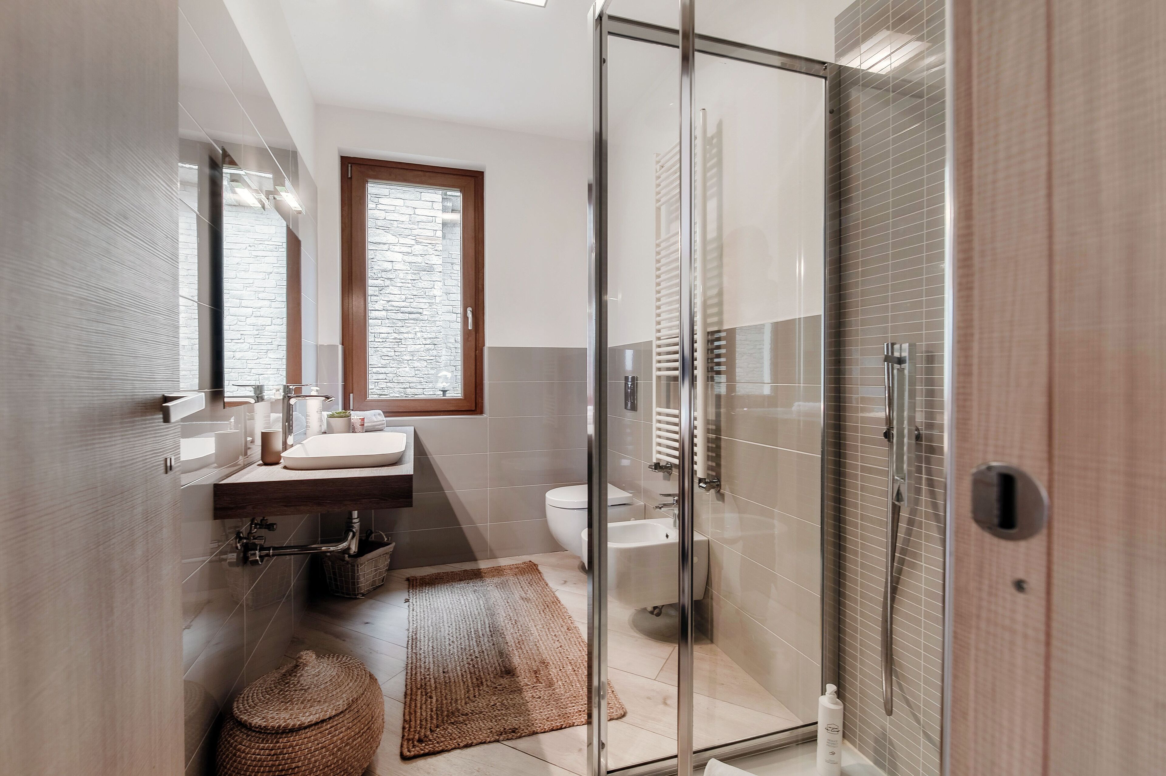 A modern bathroom with a glass shower enclosure, a sink with a mirror, a toilet, and a window.