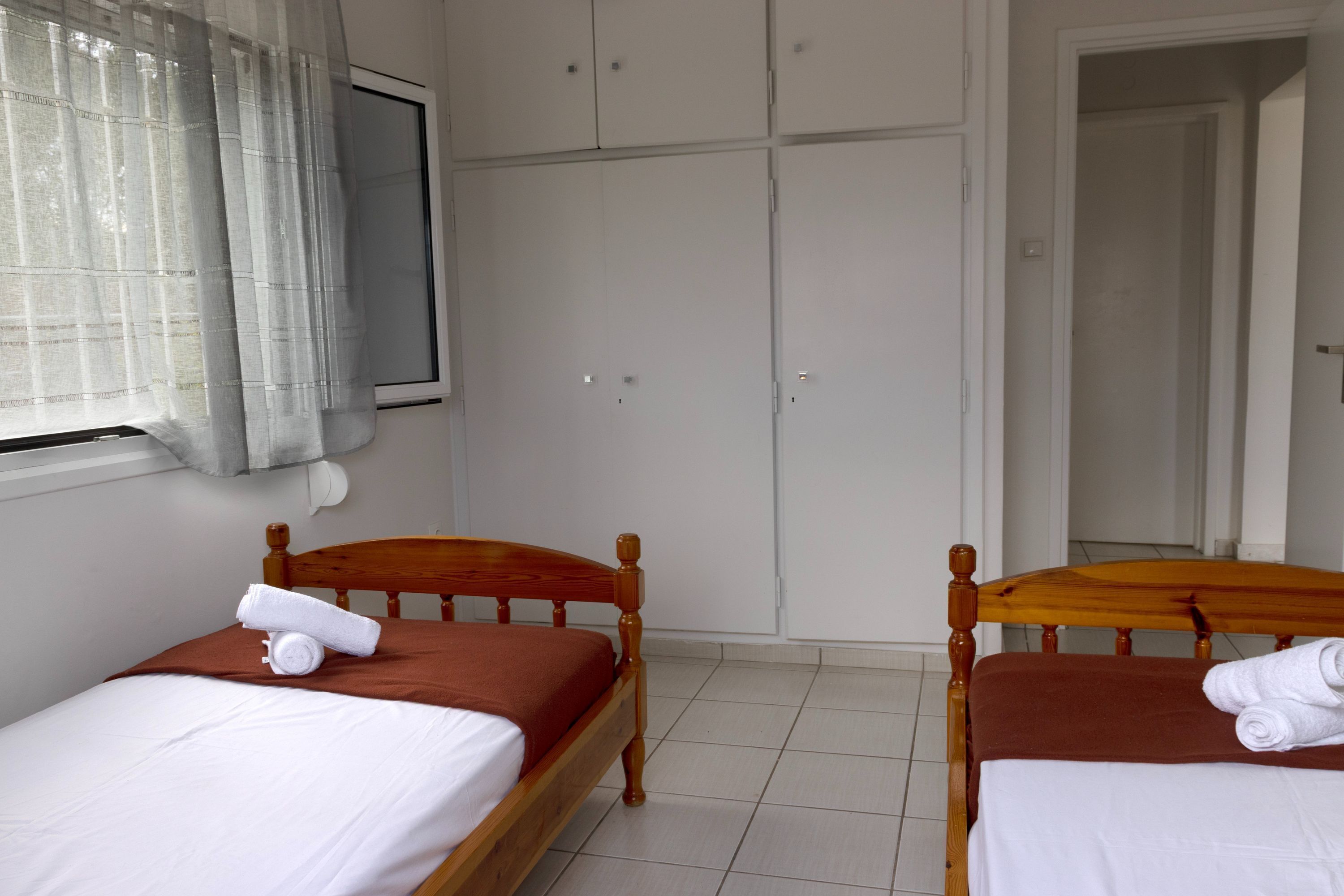 Una habitación con dos camas de madera, sábanas blancas y colchas marrones.