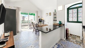 A compact kitchen with a central island, a dining area with chairs, and a view through a door to an outdoor space.