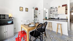 A compact kitchen with white cabinets, a wooden dining table, and a red stool.