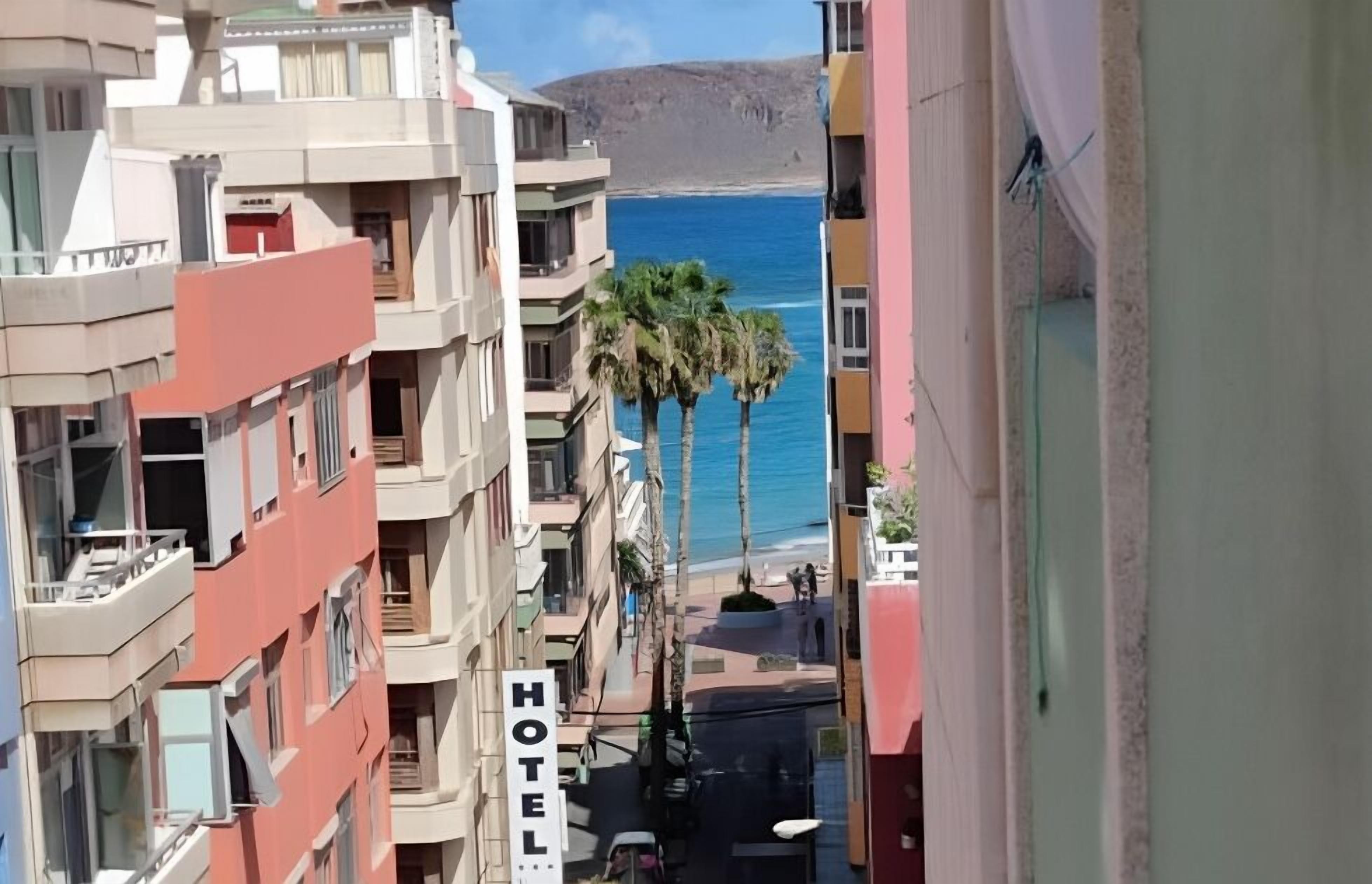 A hotel with balconies overlooking a beach and palm trees.