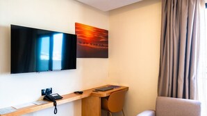 A hotel room with a flat-screen TV, a desk with a chair, a small table, and a sofa. - Hotel Unico Maarif (Casablanca)