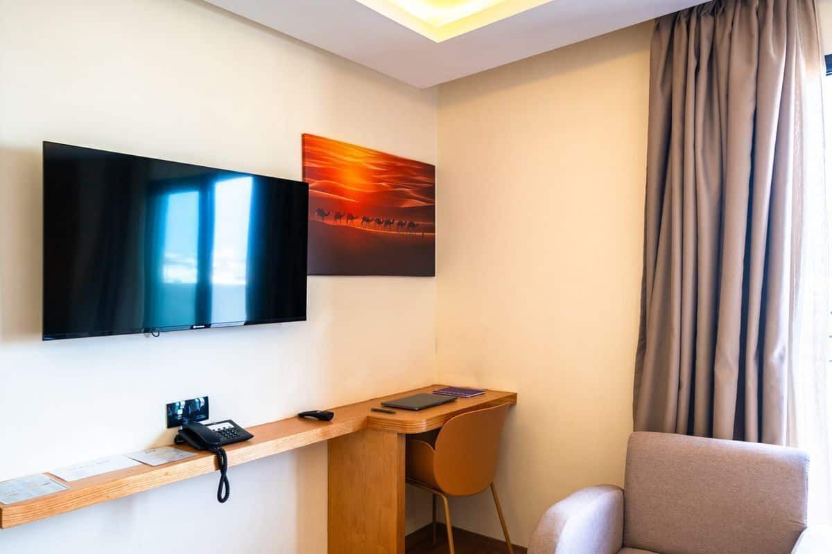 Ein Hotelzimmer mit Flachbildfernseher, Schreibtisch mit Stuhl, einem kleinen Tisch und einer Sitzecke.