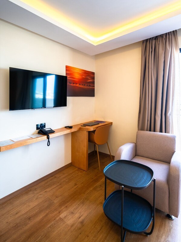 Habitación de hotel con televisor de pantalla plana, un escritorio con silla, una mesita y un sofá.