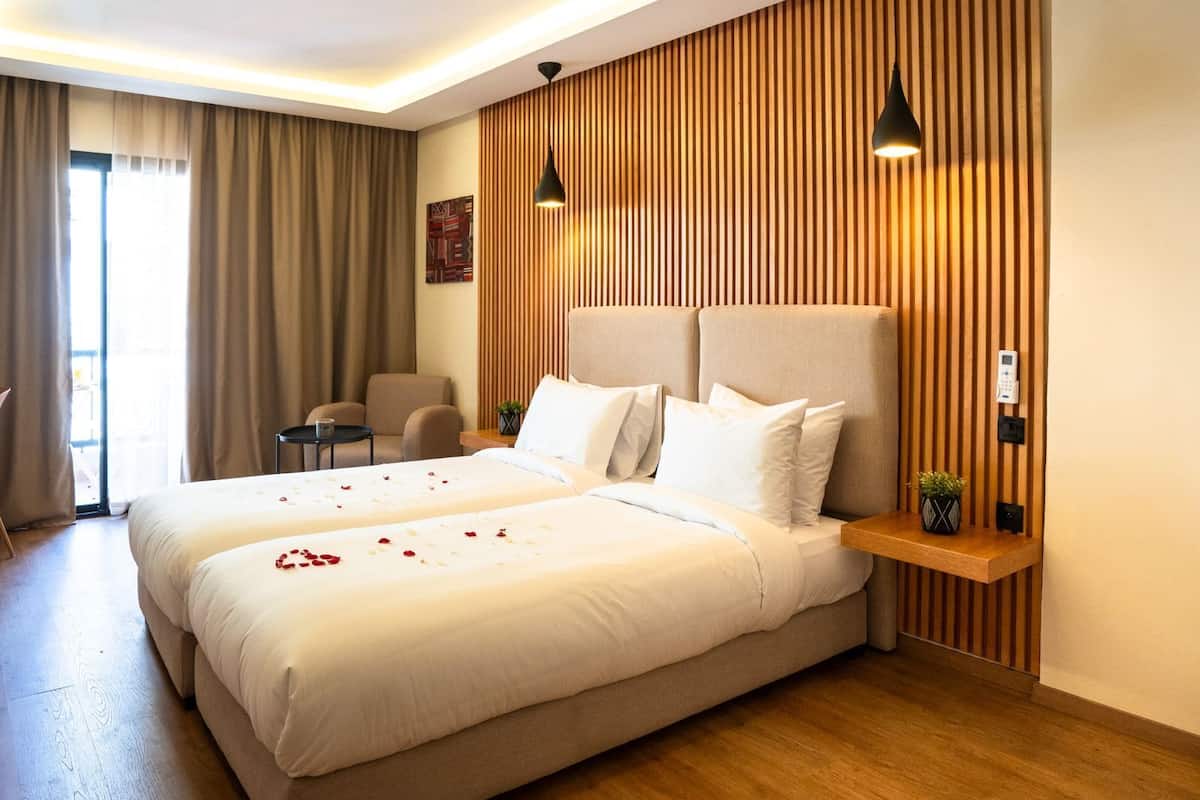 Ein Hotelzimmer mit einem großen Bett, zwei Nachttischen, einem Sessel, einem Schreibtisch und einer Wandpaneele aus Holz.