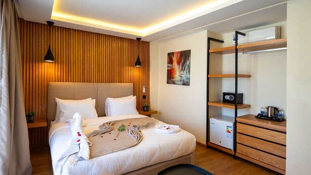 Una habitación de hotel moderna con una cama grande, lámparas de noche, un escritorio con computadora y un armario.