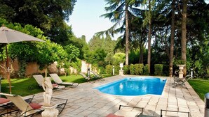 Una piscina con sillas de descanso y sombrillas, rodeada de follaje y árboles.