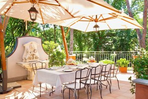 Eine Terrasse im Freien mit Esstisch und Stühlen, beschattet durch einen großen Sonnenschirm.