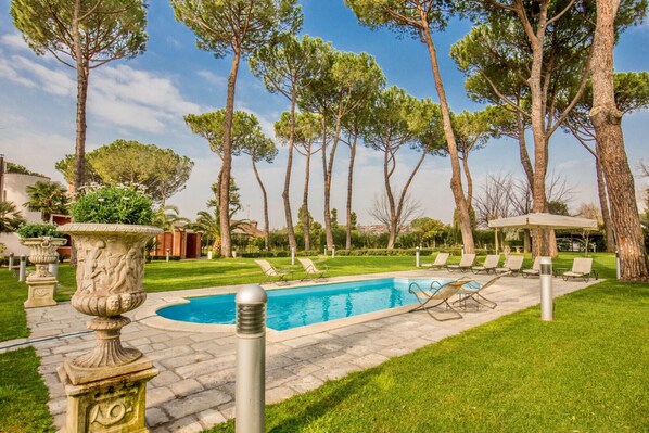 Ein Swimmingpool, umgeben von einer gepflegten Rasenfläche, mit Liegestühlen und einer Pergola.