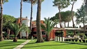 Un jardín bien cuidado con palmeras, un sendero y un edificio de fachada roja y tejado blanco.