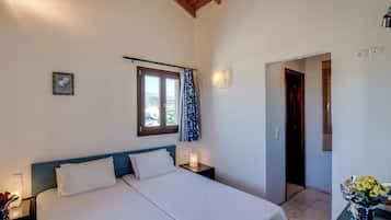 Un dormitorio con cama, mesitas de noche, una ventana con cortinas, una lámpara de pared y una puerta que da a otra habitación.