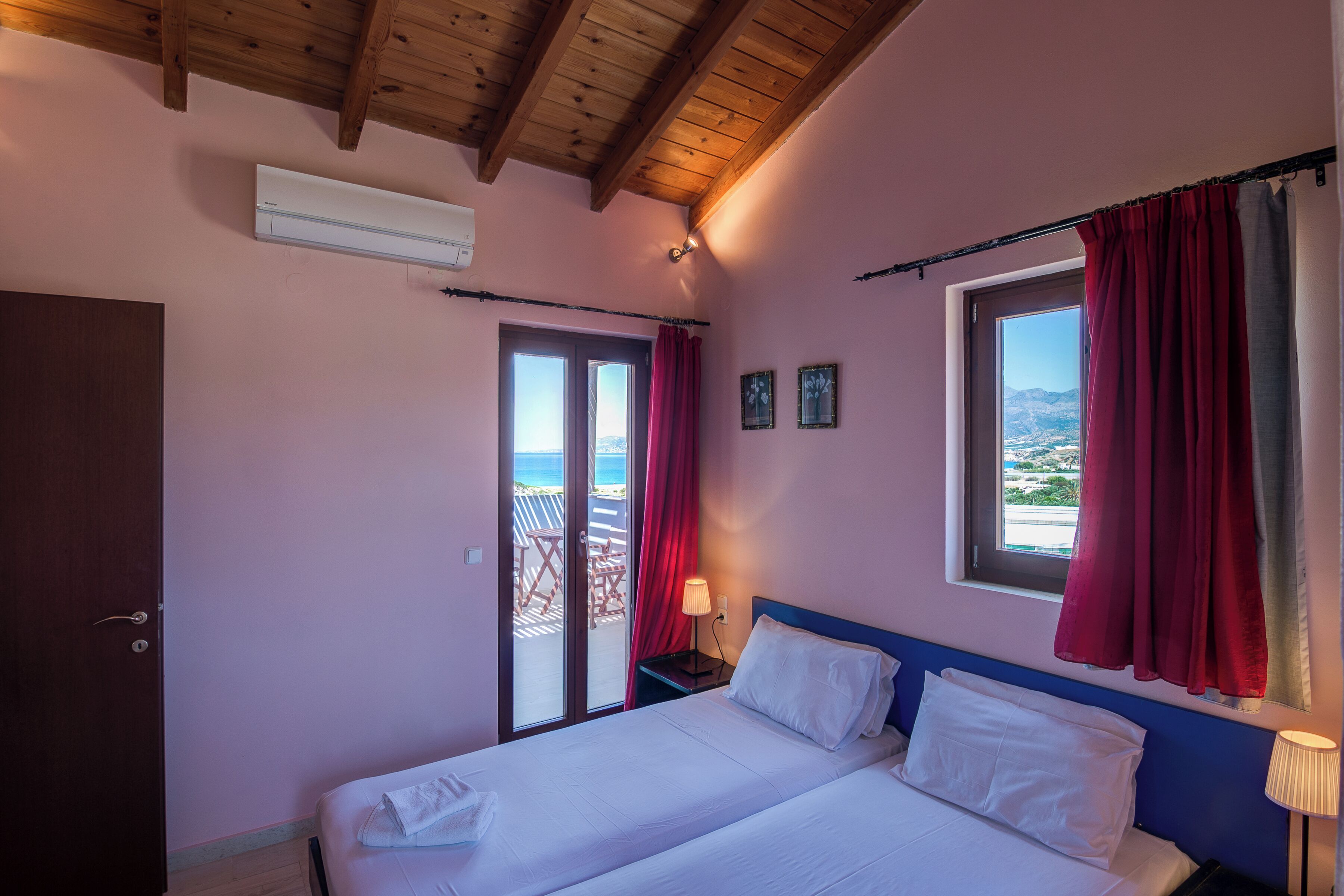Camera da letto con un letto, un comodino, una finestra con tende, una porta e vista sull'esterno.