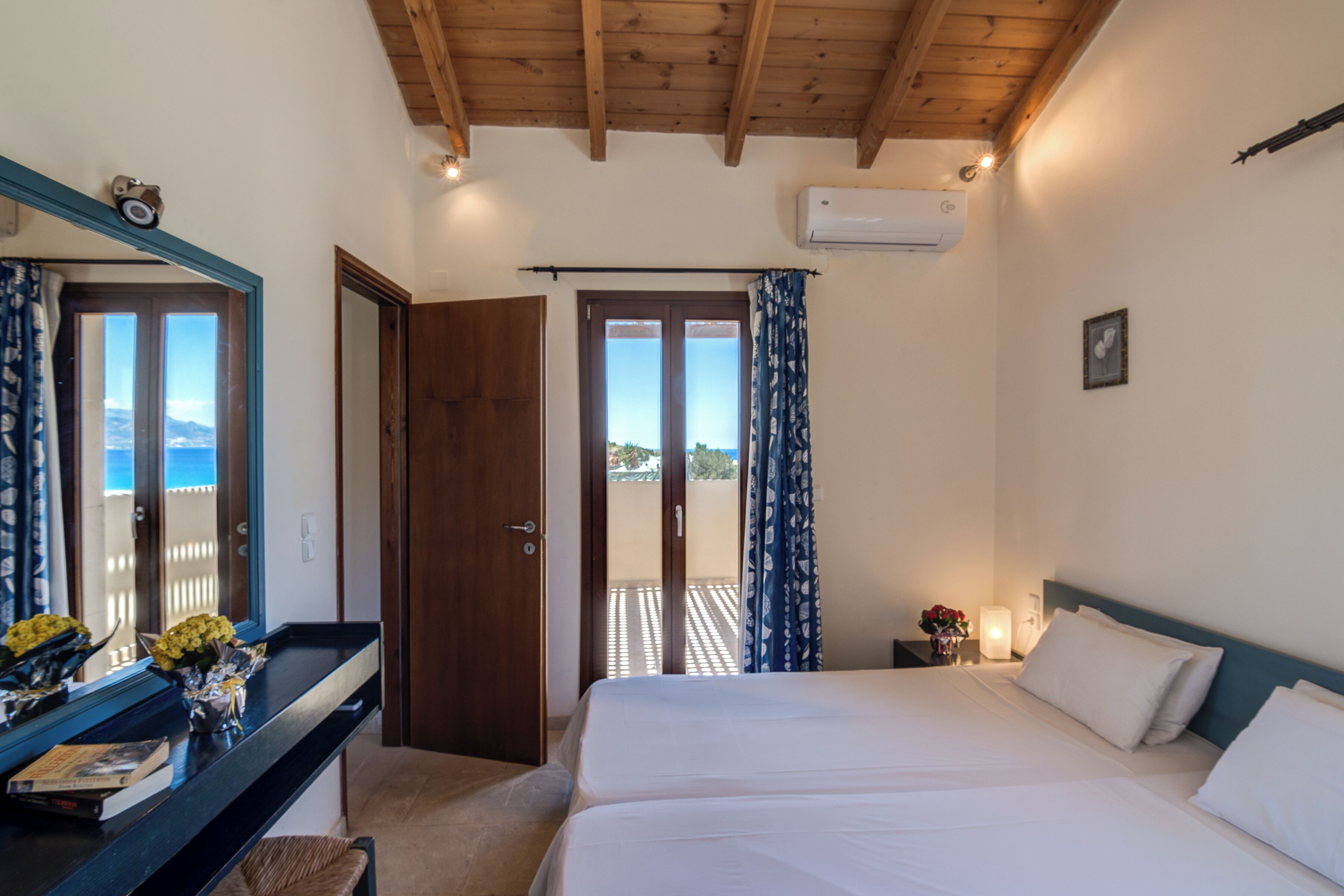 A bedroom with a bed, a desk, a mirror, and a door leading to a balcony.