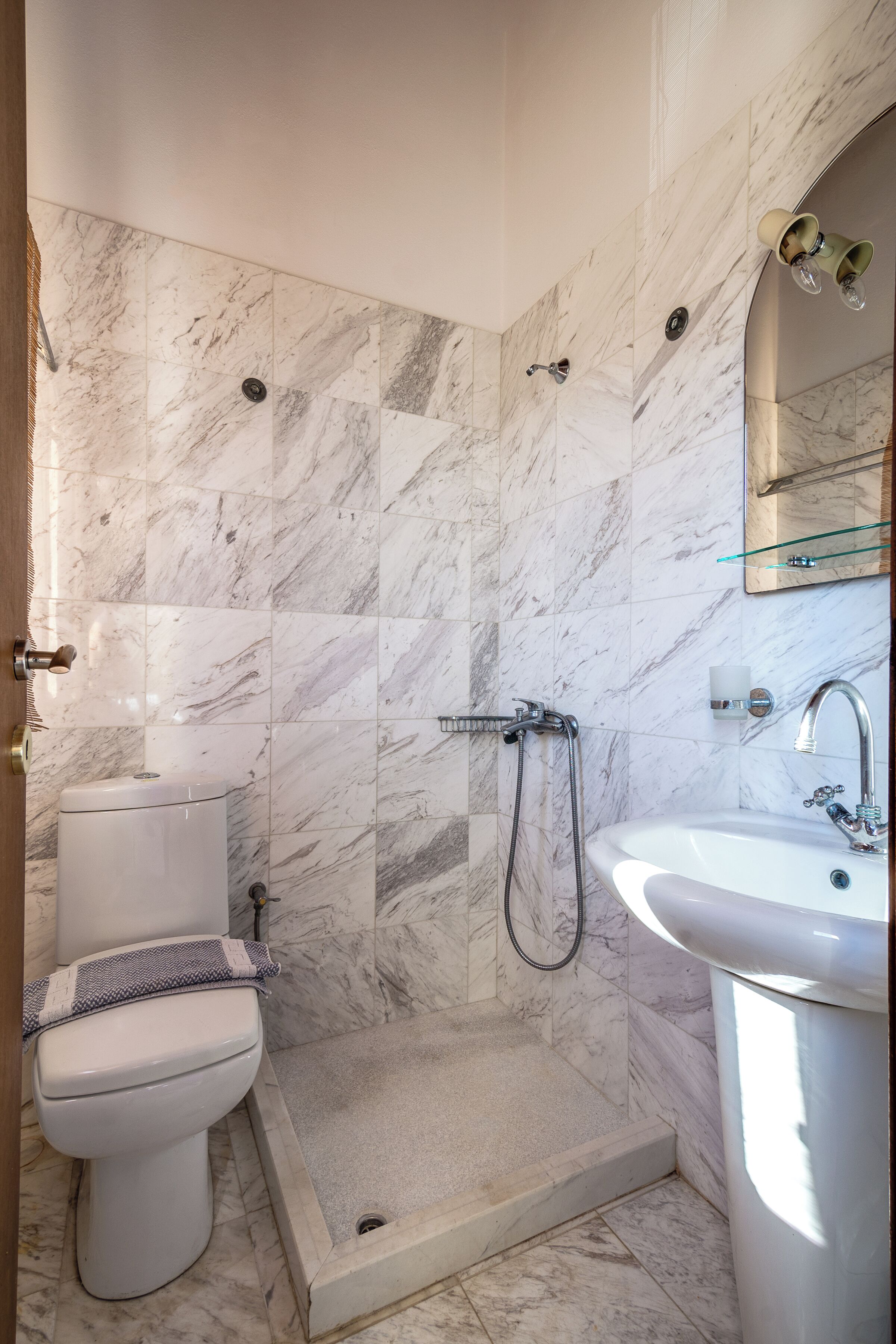 A bathroom with a toilet, shower, and sink, all with marble tiles.