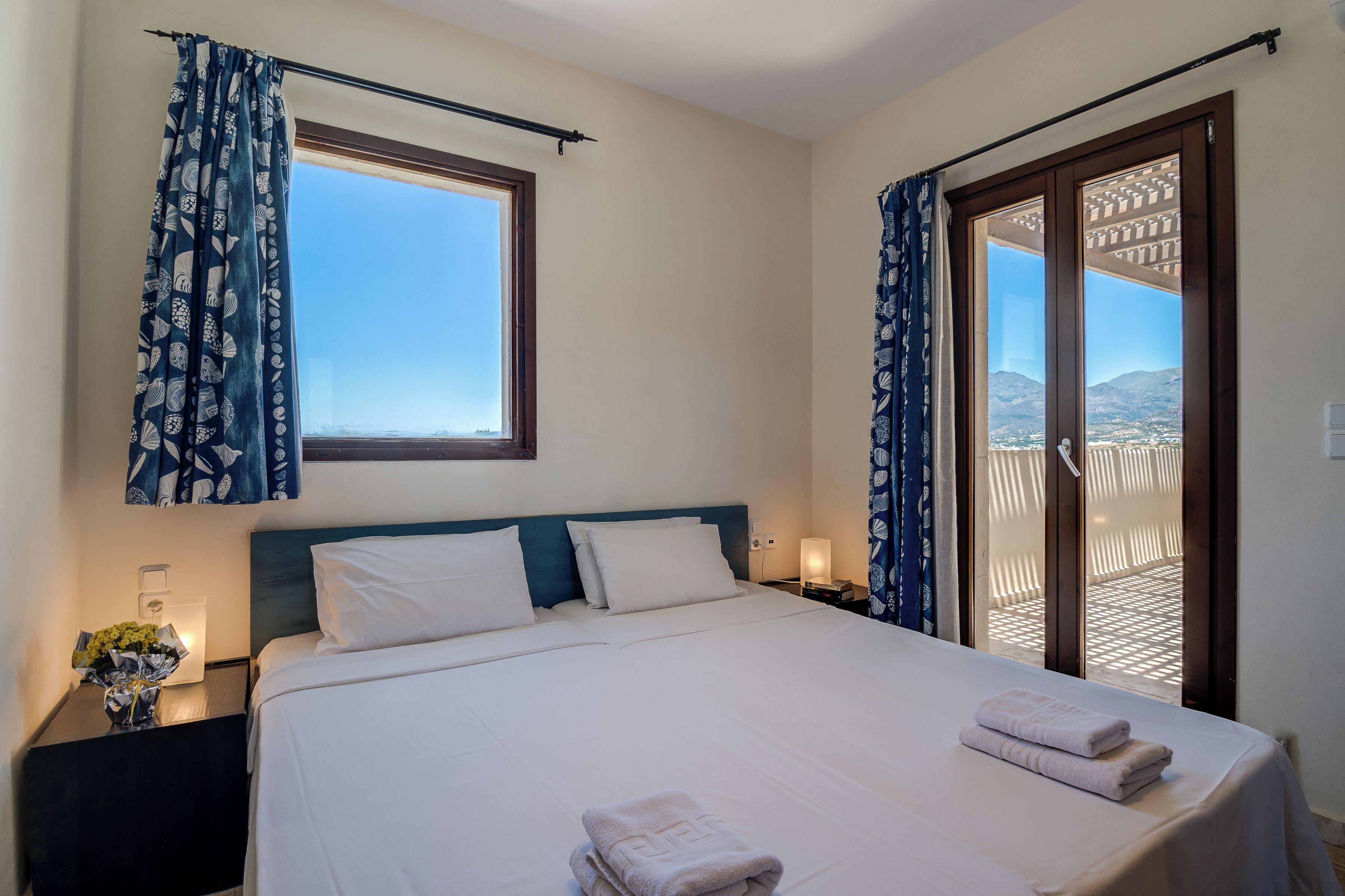 Une chambre d’hôtel avec un lit, une table de chevet, une lampe et une vue sur l’extérieur par une porte.