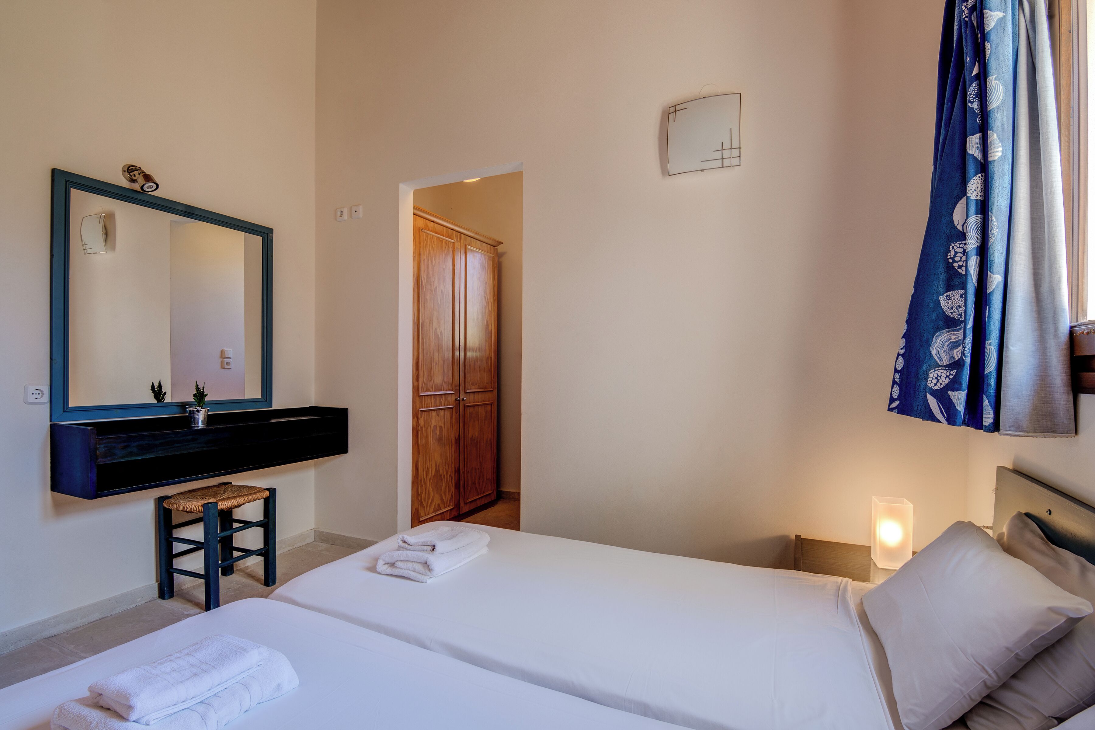 A hotel room with a bed, a nightstand, a mirror, a wooden wardrobe, and a bathroom area.