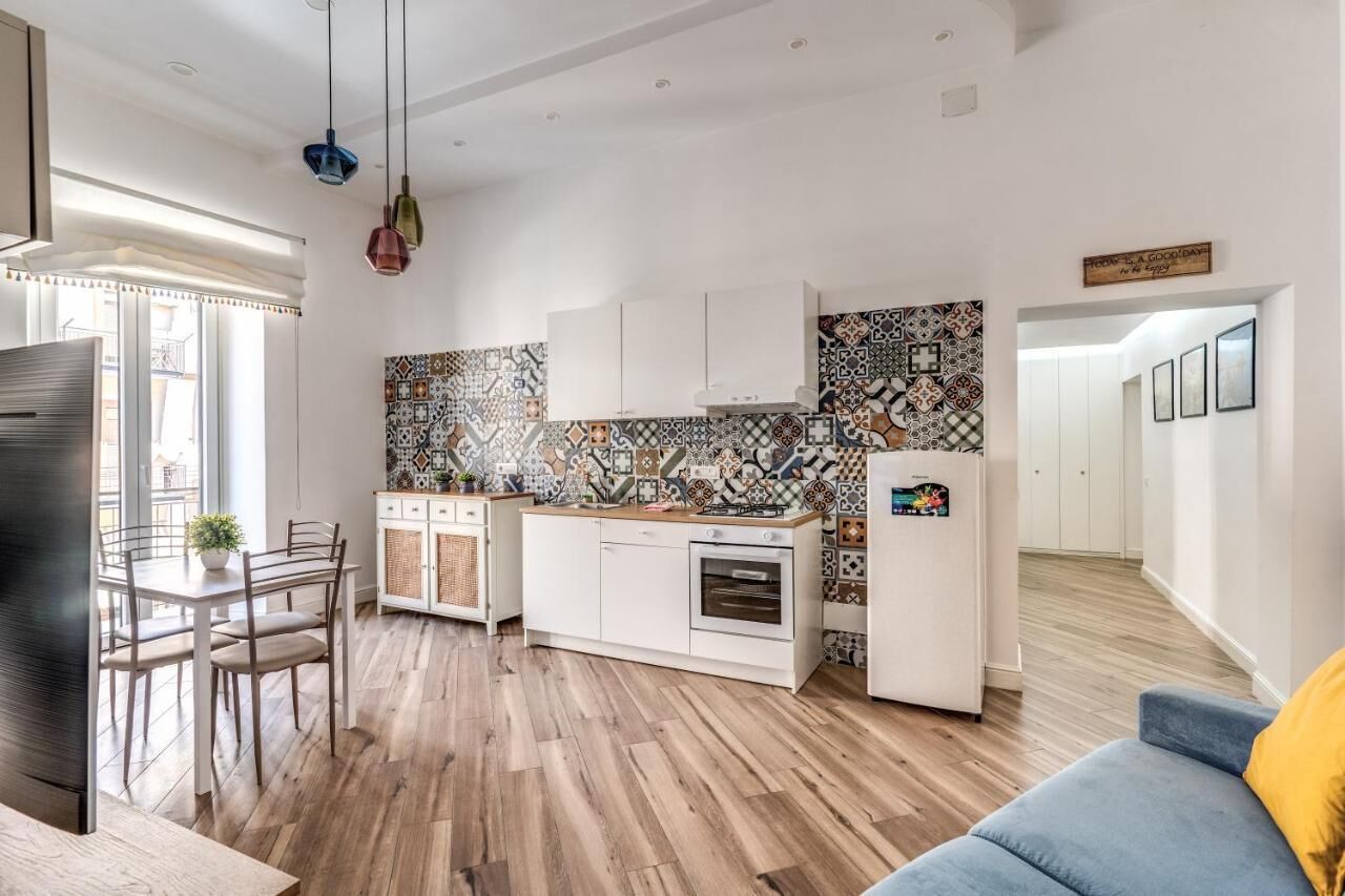 A modern kitchen with white cabinets, a patterned backsplash, and a dining area with a table and chairs.