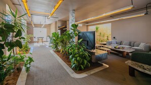 Een moderne woonkamer met een bank, salontafel en televisie. Er staan planten langs de wanden en er ligt een vloerkleed.