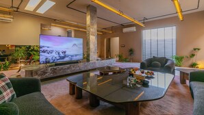 Een moderne woonkamer met een grote flatscreen televisie, een glazen salontafel en comfortabele zitplaatsen.