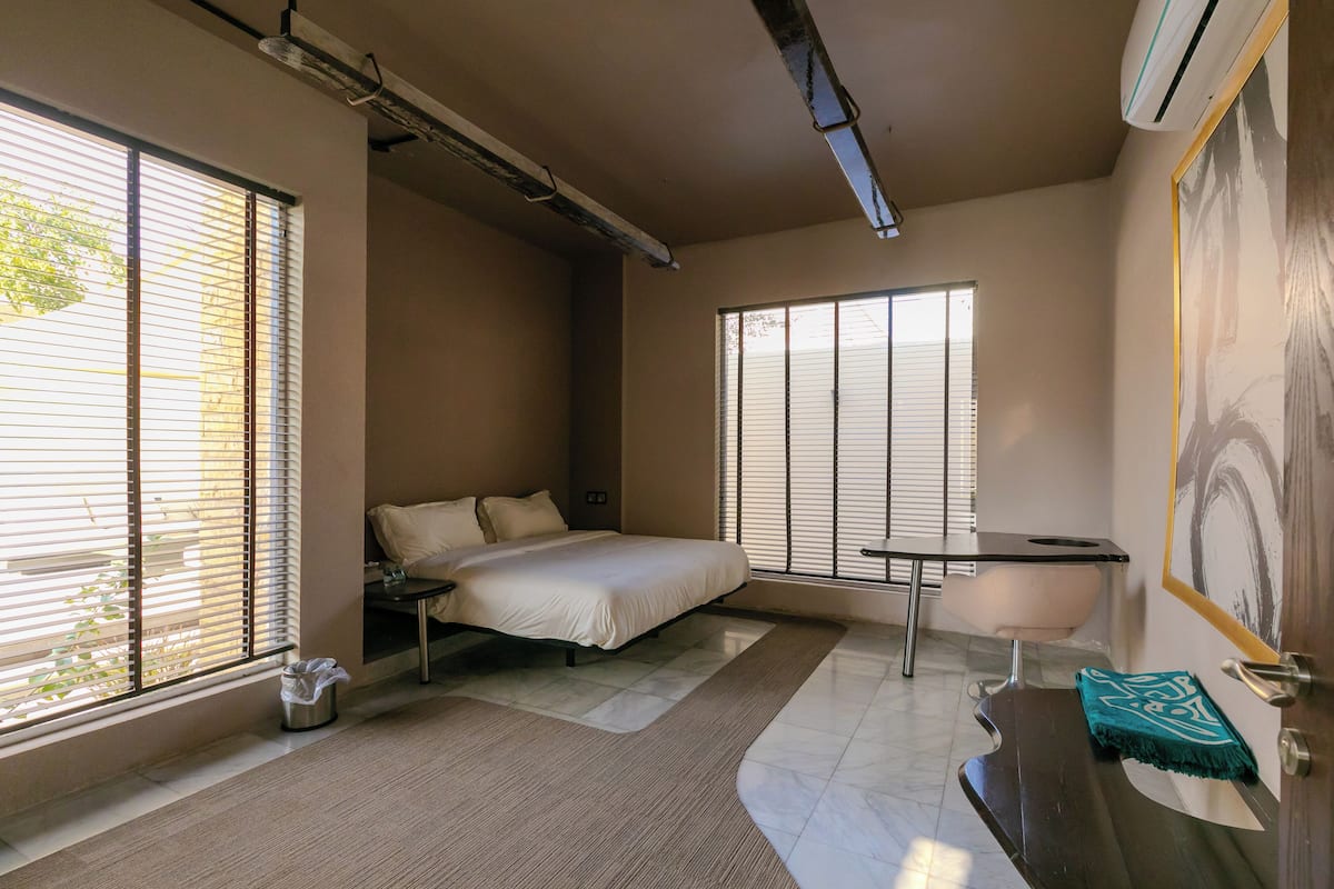A bedroom with a bed, bedside table, and a window with blinds.