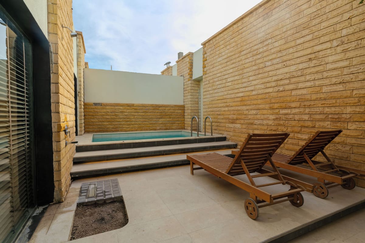 A pool area with a brick wall, a small pool, and two lounge chairs.