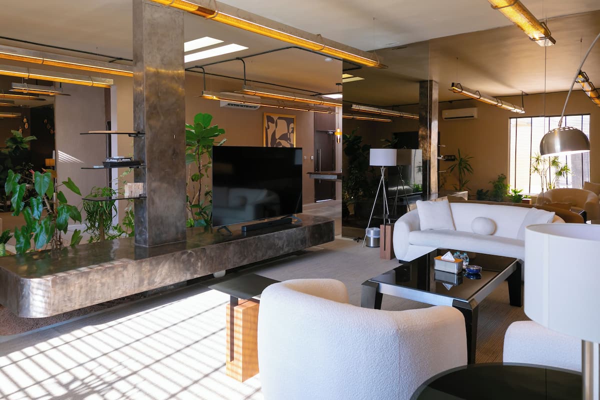 A modern living room with a flat-screen TV, white sofas, a coffee table, and potted plants.