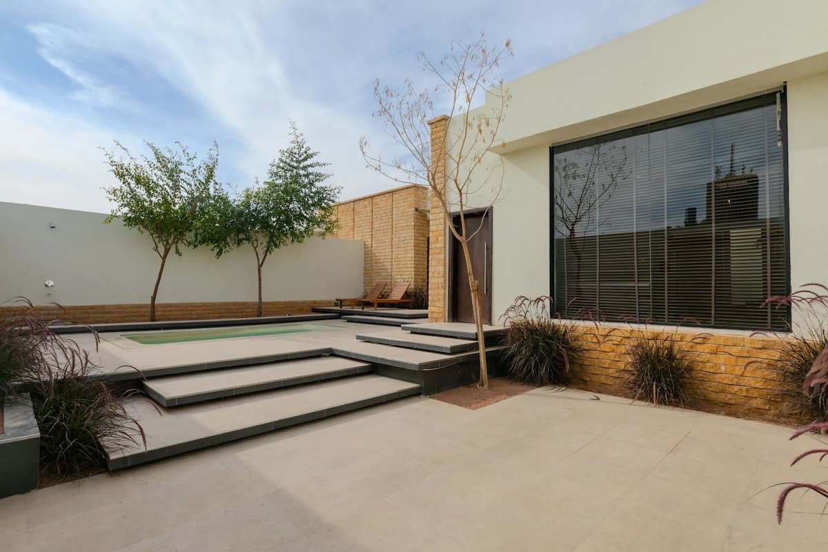A modern outdoor patio with a pool, steps leading to a door, and a large window.