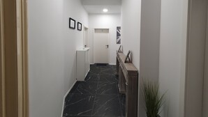 Un corridoio con pareti bianche, pavimento in marmo, una panca di legno e una porta con il numero 2.