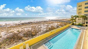 En pool med utsikt över stranden och havet, en gul vägg och en byggnad med balkonger.