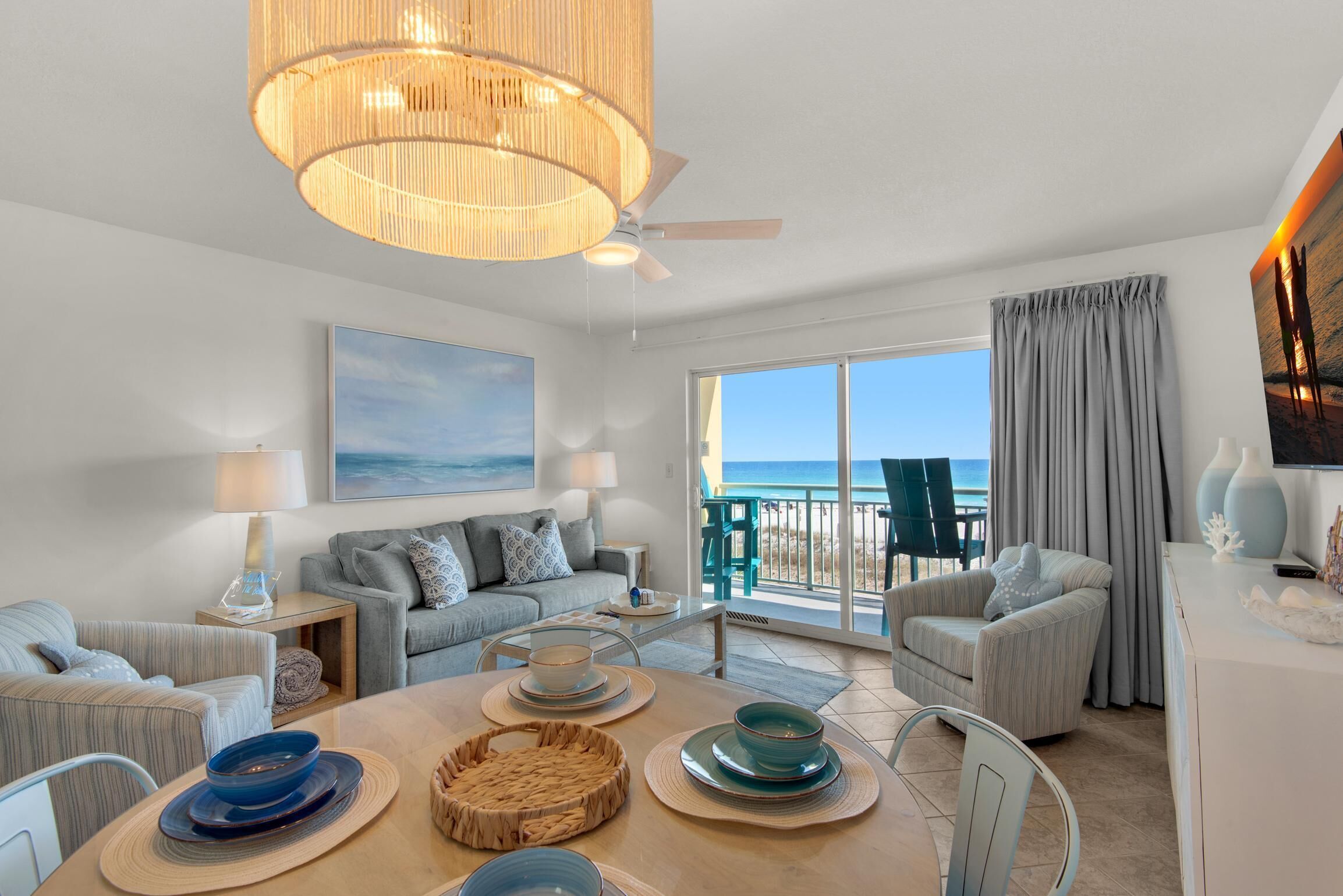 Ein großzügiges Wohnzimmer mit einem großen Fenster mit Blick auf den Strand, ein Essbereich mit einem Holztisch und ein Balkon mit Sitzgelegenheiten.