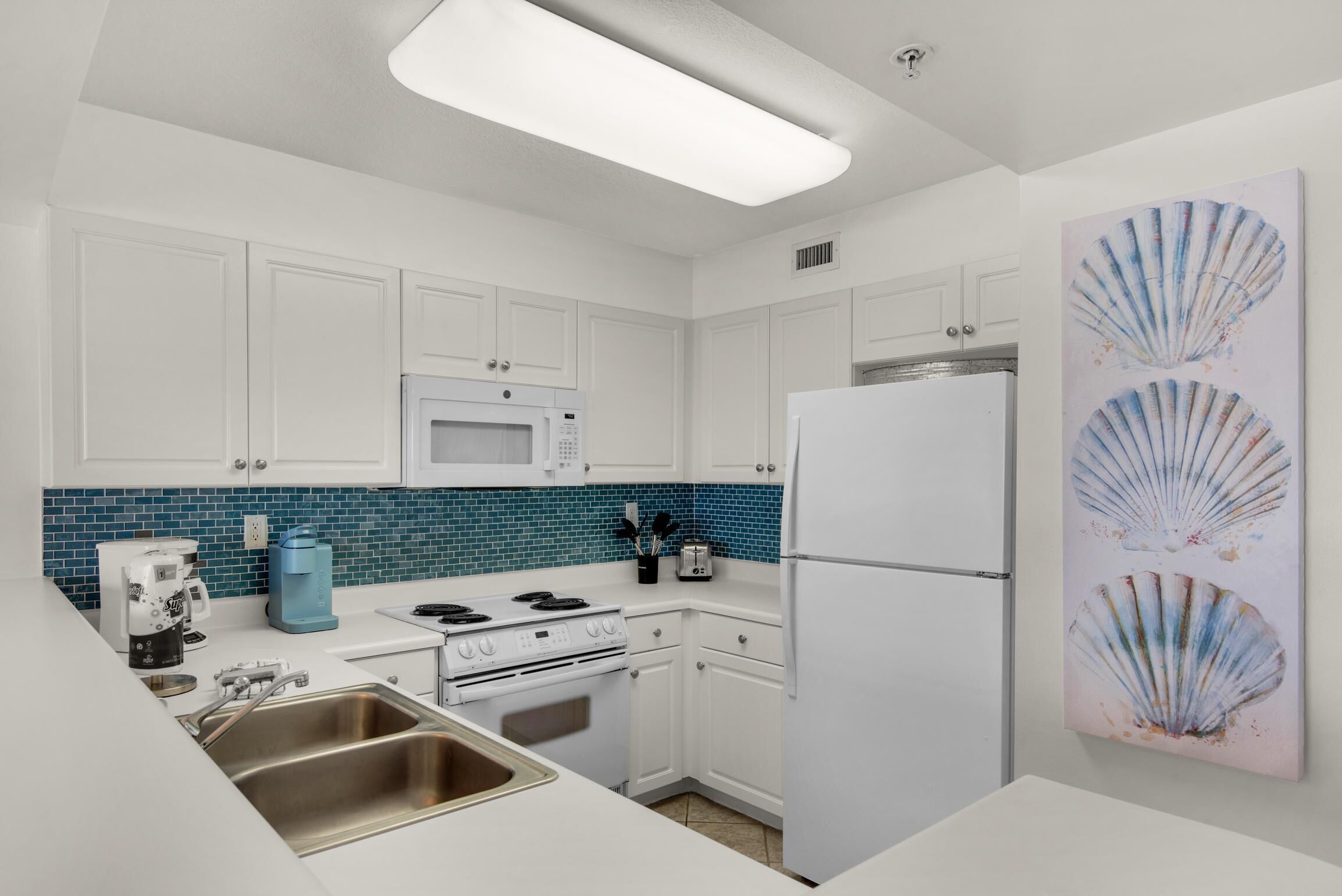 A modern kitchen with white cabinets, a blue tiled backsplash, a microwave, a stove, a sink, and a refrigerator.