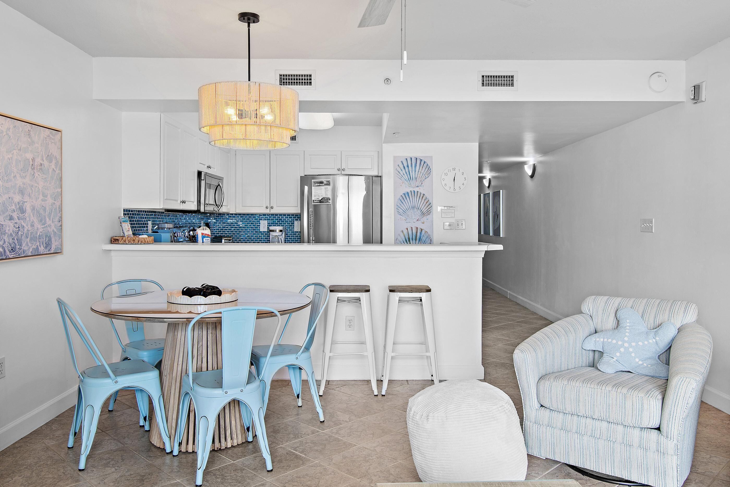 Una cocina moderna con armarios blancos, salpicadero de azulejos azules, electrodomésticos de acero inoxidable y una isla central con taburetes.