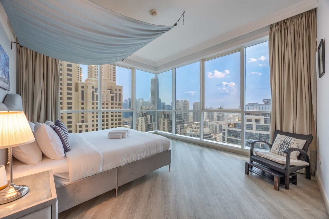 A hotel room with a large bed, a chair, a desk, and a view of the cityscape.