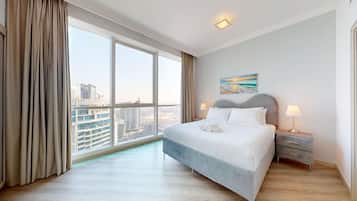 Une chambre d’hôtel moderne dotée d’une grande fenêtre donnant sur la ville, d’un lit soigneusement fait et d’une petite table de chevet avec une lampe.