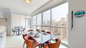 Un'area pranzo moderna con tavolo in vetro, sedie arancioni e vista sulla città attraverso ampie finestre.