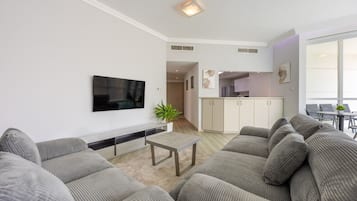 Een moderne woonkamer met een flatscreen televisie, grijze banken, een salontafel en een keuken op de achtergrond.