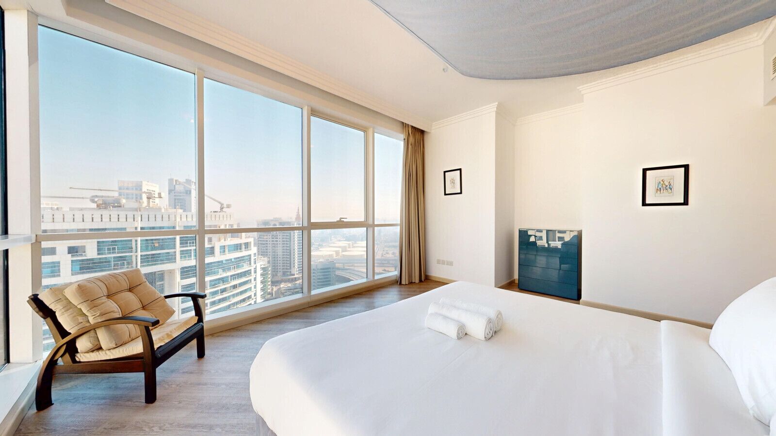 A hotel room with a large bed, a chair, a TV, and a city view.