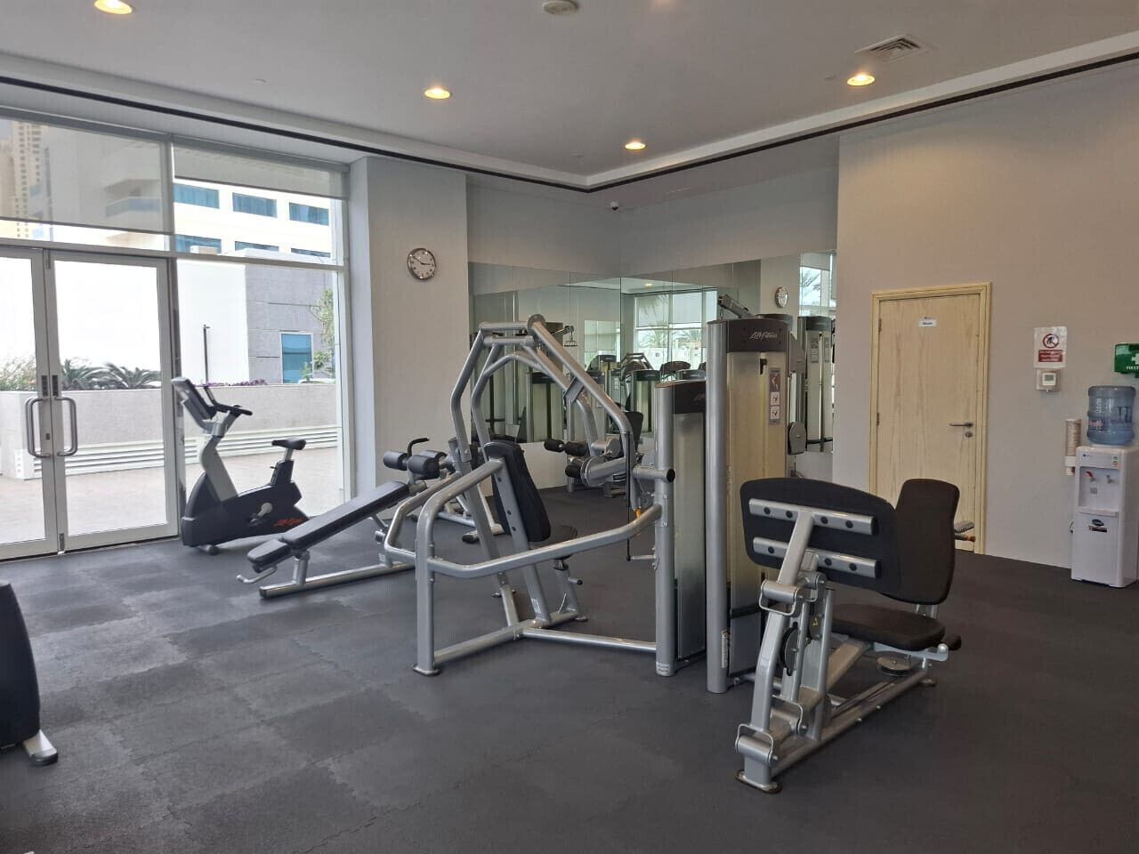 A gym with exercise equipment, a water dispenser, and a view of the outside.