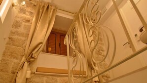 Ένα μπάνιο με έναν τοίχο από πέτρα, ένα παράθυρο με μεταλλικό πλαίσιο και κουρτίνες και μια κρεμάστρα για πετσέτες.